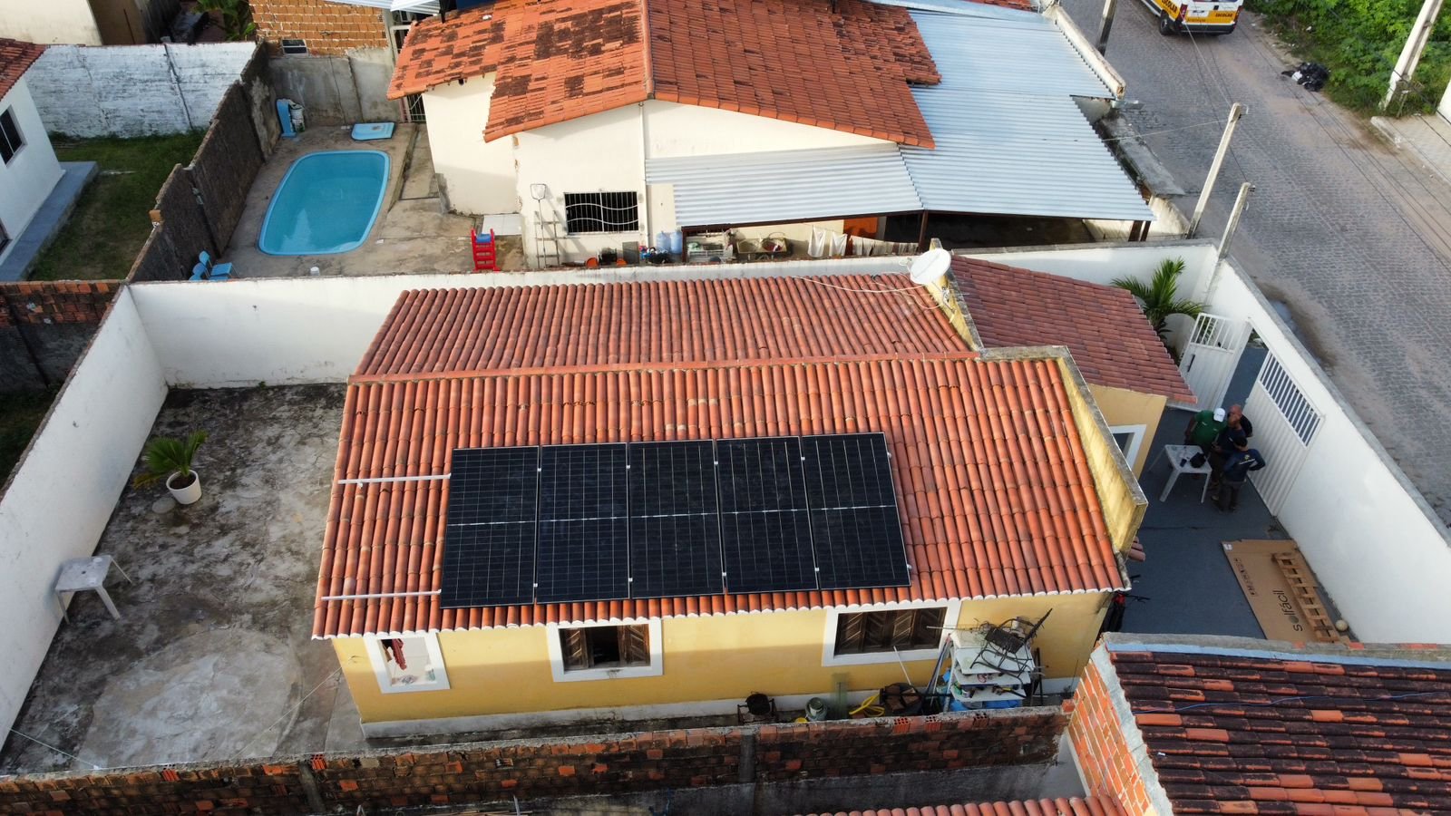 Vista de drone de uma casa amarela com telhado cerâmico, módulos solares instalados e piscina no quintal, na Grande Natal.