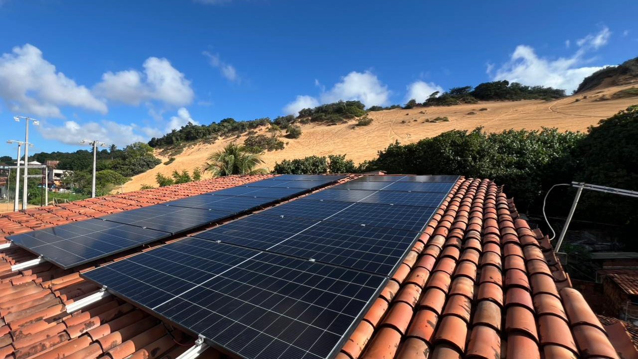 Módulos solares sobre telhado cerâmico, com dunas e céu aberto ao fundo, em uma usina residencial instalada pela LIV no Rio Grande do Norte.